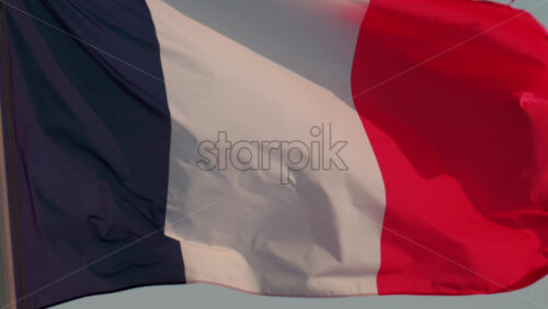 Video - A close up of the French national flag waving gracefully in the wind under a clear blue sky