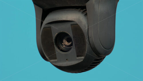 Video - A close up of a modern black surveillance camera turning against a bright sky background