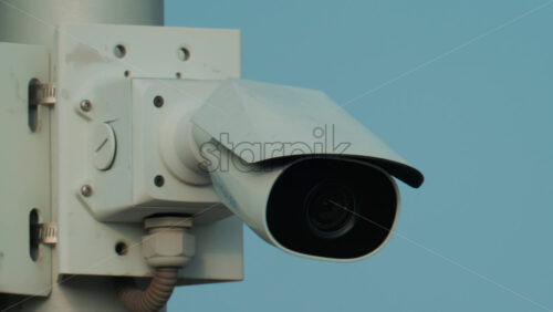 Video - A close up of a modern black surveillance camera turning against a bright sky background