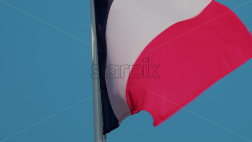 Video - A close up of the French national flag waving gracefully in the wind under a clear blue sky
