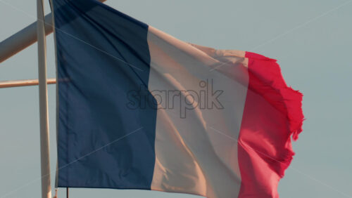 Video - A close up of the French national flag waving gracefully in the wind under a clear blue sky