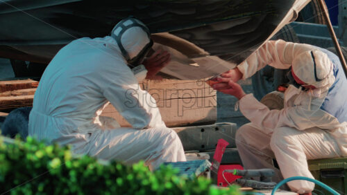 Video - Cannes, France - October 11, 2025: Two workers wearing protective white suits and respirators sand and repair the hull of a boat in dry dock