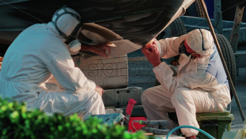 Video - Cannes, France - October 11, 2025: Two workers wearing protective white suits and respirators sand and repair the hull of a boat in dry dock