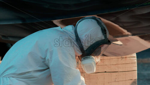 Video - Cannes, France - October 11, 2025: Two workers wearing protective white suits and respirators sand and repair the hull of a boat in dry dock