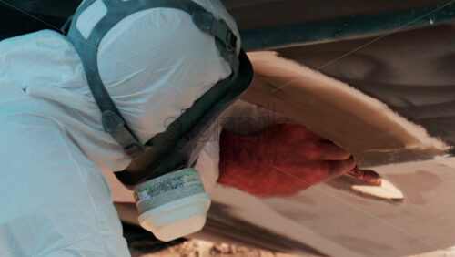 Video - Close up of a craftsman in a protective suit sanding the underside of a boat