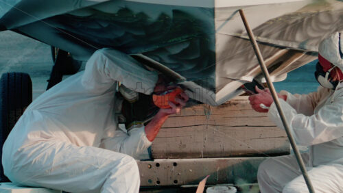 Video - Cannes, France - October 11, 2025: Two workers wearing protective white suits and respirators sand and repair the hull of a boat in dry dock