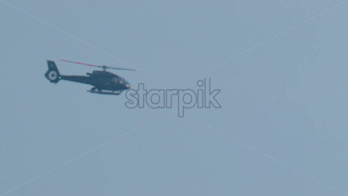 Video - A black helicopter flies across a clear blue sky in bright daylight
