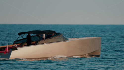 Video - A sleek beige motorboat glides across calm blue waters with sunlight reflecting off its hull