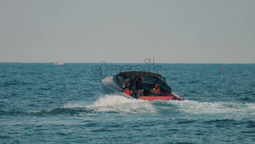 Video - A luxury boat with a black canopy and red interior speeds across open sea, leaving a white trail of waves behind