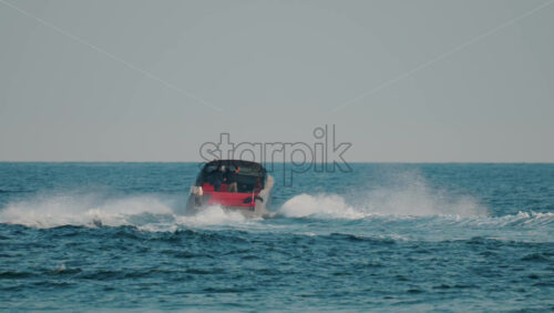 Video - A luxury boat with a black canopy and red interior speeds across open sea, leaving a white trail of waves behind