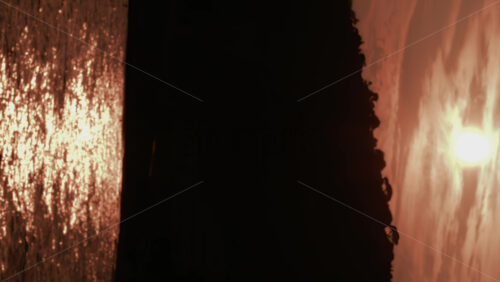Video - A dramatic sunset view showing a dark cliff silhouette with golden sunlight shimmering across the sea. Vertical