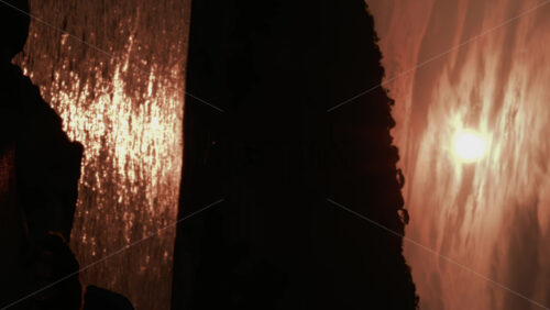 Video - A dramatic sunset view showing a dark cliff silhouette with golden sunlight shimmering across the sea. Vertical