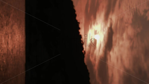 Video - A dramatic sunset view showing a dark cliff silhouette with golden sunlight shimmering across the sea. Vertical