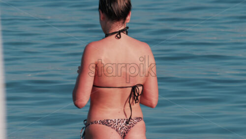 Video - A woman stands waist deep in the calm sea, wearing a leopard pattern bikini under the warm sun