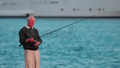 Video - Cannes, France - October 11, 2025: An elderly man fishes calmly by the seaside, holding his fishing rod as he looks toward the horizon