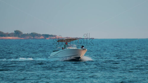 Video - Cannes, France - October 11, 2025: A small white motorboat with passengers moves across calm blue water near the coastline