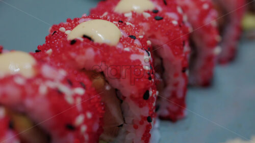 Video - Close up of vibrant red sushi rolls topped with creamy sauce and sesame seeds, served on a ceramic plate