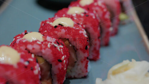 Video - Close up of vibrant red sushi rolls topped with creamy sauce and sesame seeds, served on a ceramic plate