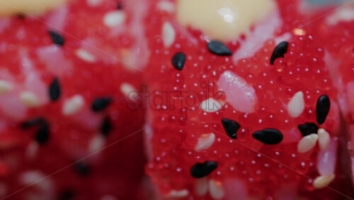Video - Close up of vibrant red sushi rolls topped with creamy sauce and sesame seeds, served on a ceramic plate