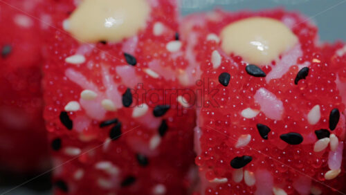 Video - Close up of vibrant red sushi rolls topped with creamy sauce and sesame seeds, served on a ceramic plate