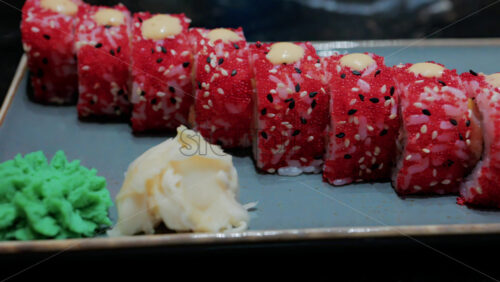 Video - Close up of vibrant red sushi rolls topped with creamy sauce and sesame seeds, served on a ceramic plate