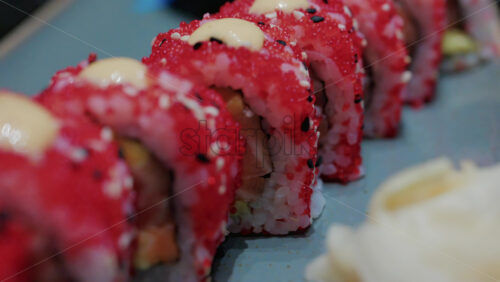 Video - Close up of vibrant red sushi rolls topped with creamy sauce and sesame seeds, served on a ceramic plate