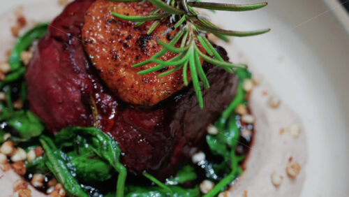Video - Close up of a gourmet dish featuring grilled steak topped with foie gras, served with sauteed spinach and a rosemary garnish