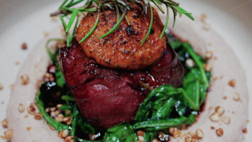 Video - Close up of a gourmet dish featuring grilled steak topped with foie gras, served with sauteed spinach and a rosemary garnish
