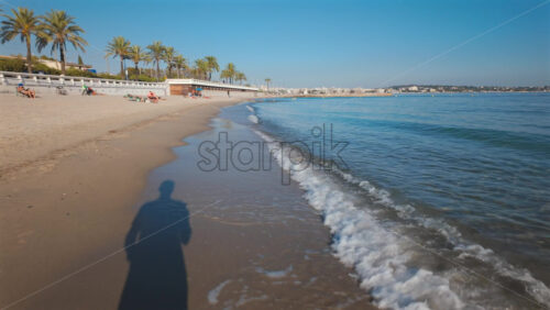 Video - View of waves washing up on sandy shore with a man's shadow visible