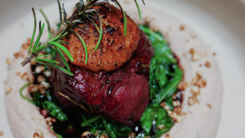 Video - Close up of a gourmet dish featuring grilled steak topped with foie gras, served with sauteed spinach and a rosemary garnish