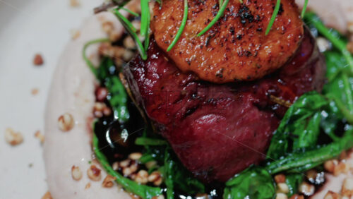 Video - Close up of a gourmet dish featuring grilled steak topped with foie gras, served with sauteed spinach and a rosemary garnish