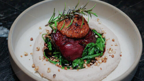 Video - Close up of a gourmet dish featuring grilled steak topped with foie gras, served with sauteed spinach and a rosemary garnish