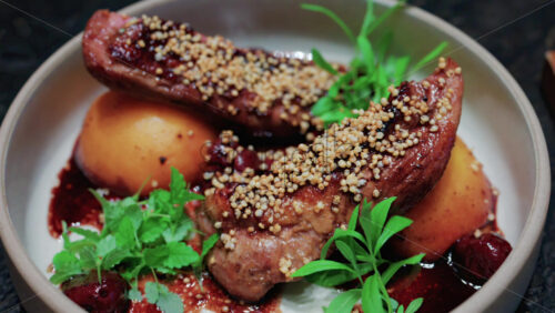 Video - Close up of roasted duck breast plated with caramelized pear, crispy grains, and green herbs
