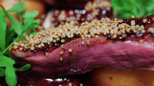 Video - Close up of roasted duck breast plated with caramelized pear, crispy grains, and green herbs