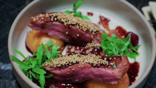 Video - Close up of roasted duck breast plated with caramelized pear, crispy grains, and green herbs