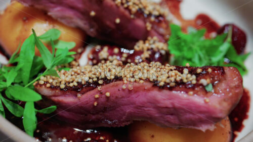 Video - Close up of roasted duck breast plated with caramelized pear, crispy grains, and green herbs