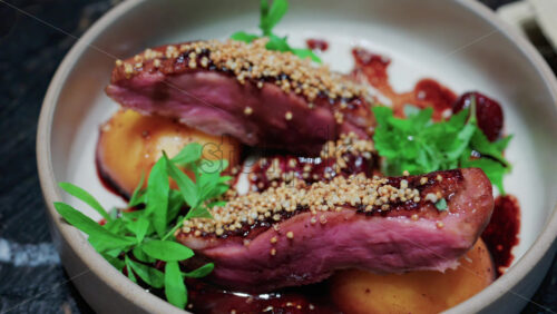 Video - Close up of roasted duck breast plated with caramelized pear, crispy grains, and green herbs