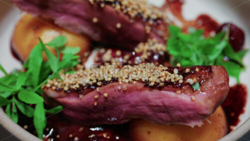 Video - Close up of roasted duck breast plated with caramelized pear, crispy grains, and green herbs