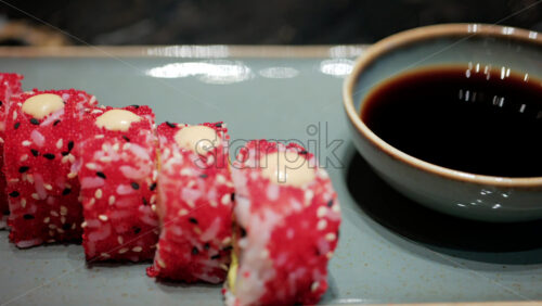 Video - Close up of vibrant red sushi rolls topped with creamy sauce and sesame seeds, served on a ceramic plate