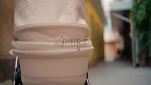 Video - Rear view of a beige baby stroller moving along a narrow alley with yellow and brown walls