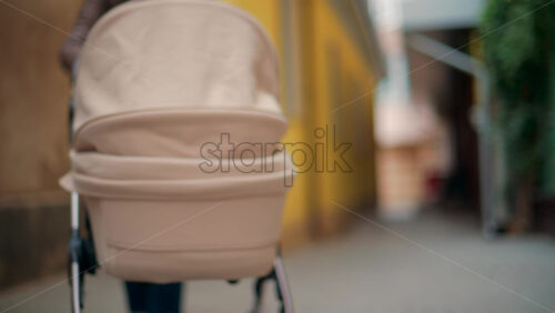 Video - Rear view of a beige baby stroller moving along a narrow alley with yellow and brown walls