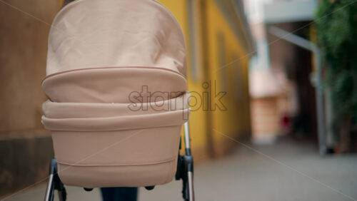Video - Rear view of a beige baby stroller moving along a narrow alley with yellow and brown walls