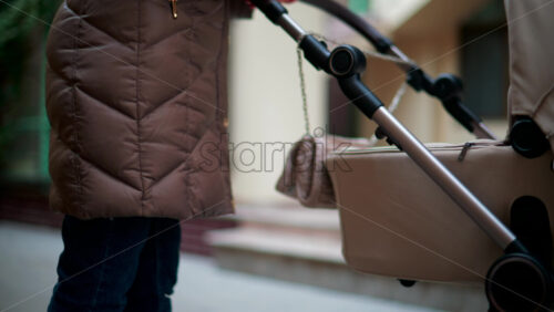 Video - Close up of a hand pushing a beige baby stroller while walking through a colorful urban street