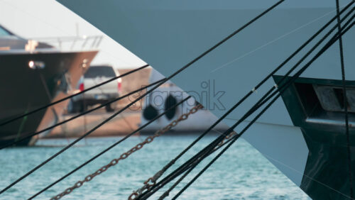 Video - Close up of ropes and metal chains securing a luxury yacht in port, with blurred water and boats in the background