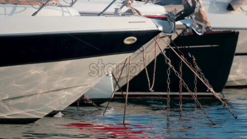 Video - Close up of ropes and metal chains securing a luxury yacht in port, with blurred water and boats in the background