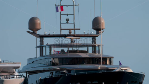 Video - Cannes, France - October 12, 2025: Front view of a luxury superyacht with antennas, radars, and flags waving under a clear blue sky