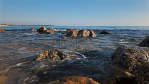 Video - View of sea waves gently washing over rocky shore under clear blue sky