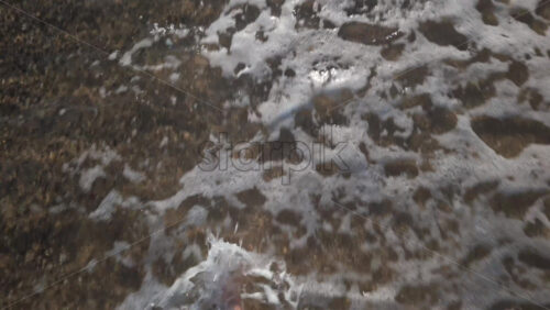 Video - Close up of a man's bare foot touching sea foam while walking on the sandy beach