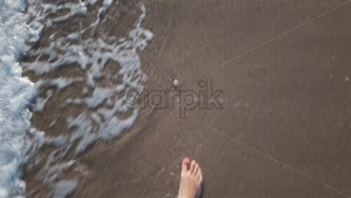 Video - Close up of a man's bare foot touching sea foam while walking on the sandy beach