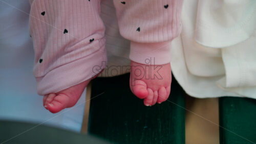Video - Close up shot of a baby's feet resting on a bench, wearing soft pink clothes with small heart patterns